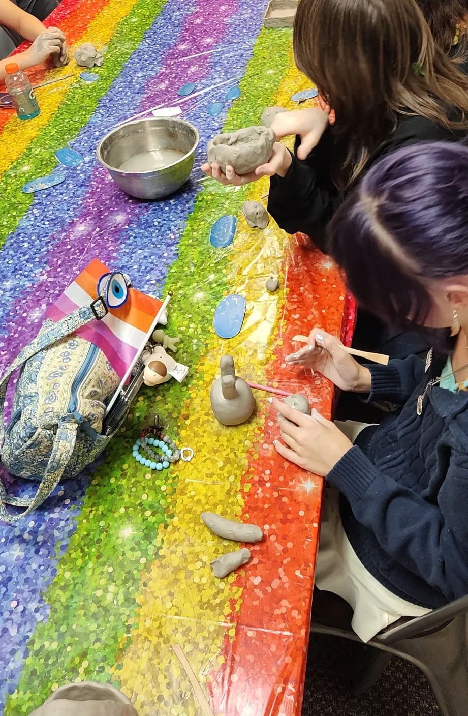 Campers shaping gray clay at a table covered in a sparkly rainbow tablecloth.