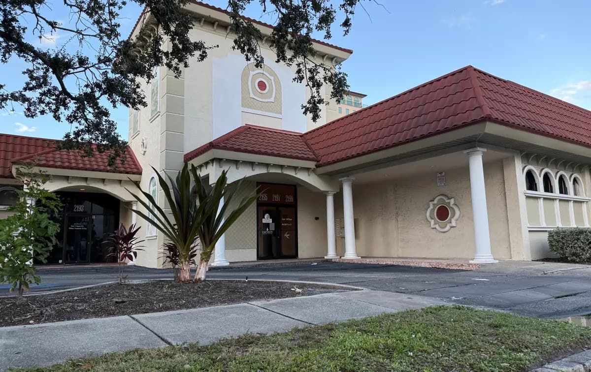 The Sarasota Center at 2195 Ringling Boulevard: a cream building with a red tile roof, white columns, and an arched entry.